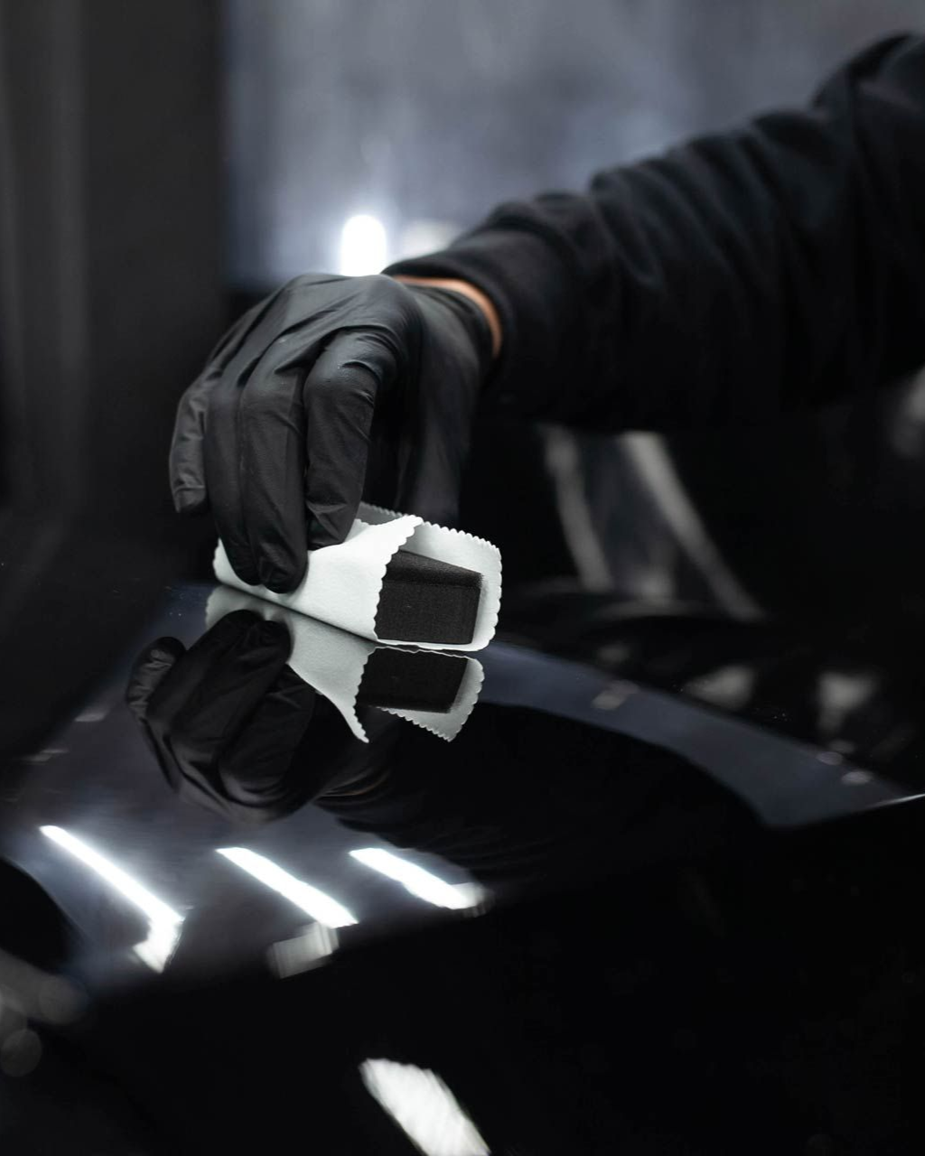 A person is using a blue squeegee to remove plastic from the hood of a car
