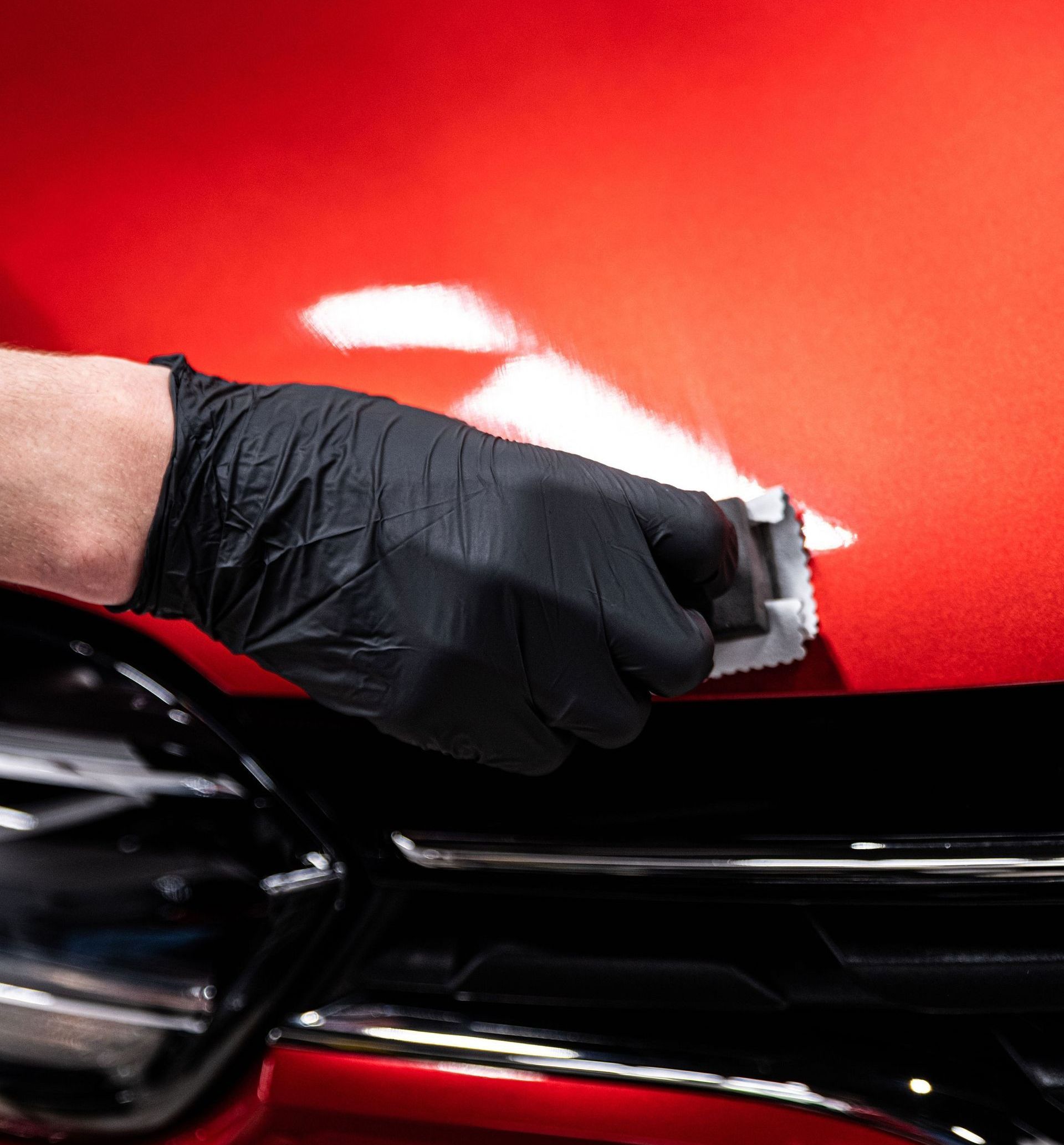 A person wearing black gloves is polishing the hood of a red car.
