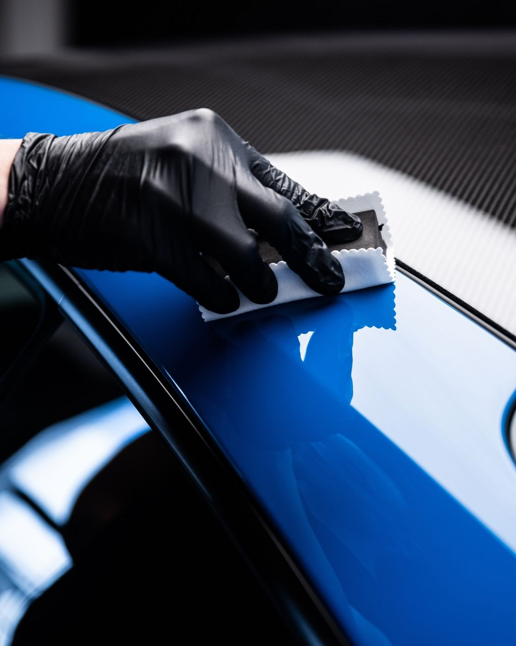 A person is applying a clear film to the hood of a car.
