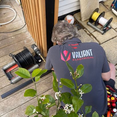 A man wearing a valiant electrical shirt is working on a deck.