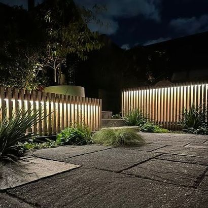 A wooden fence is lit up at night in a backyard.