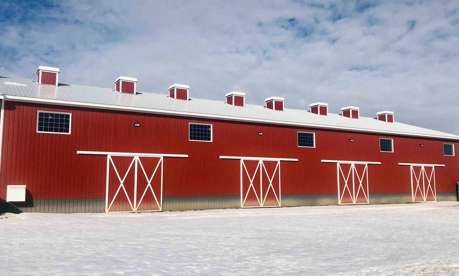 a red barn with white doors is covered in snow.