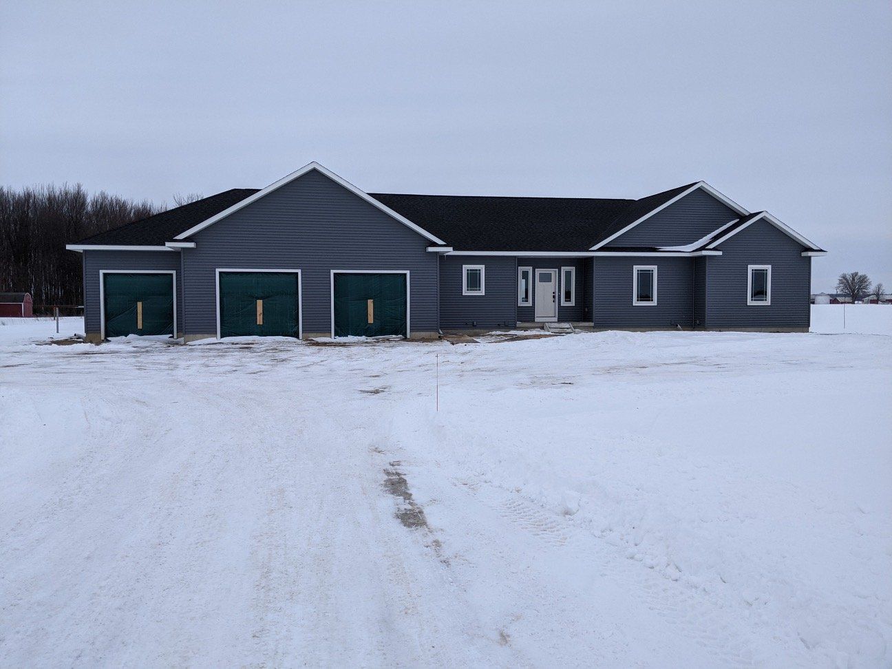 a gray house with green garage doors in a snowy field