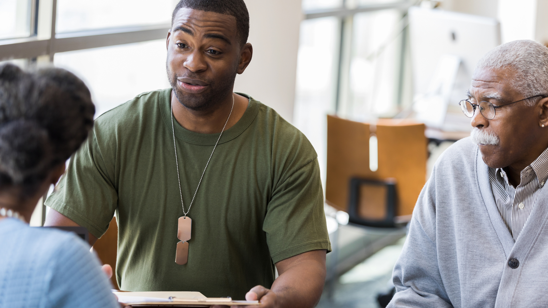 Man in green shirt talking to two people, one wearing glasses.