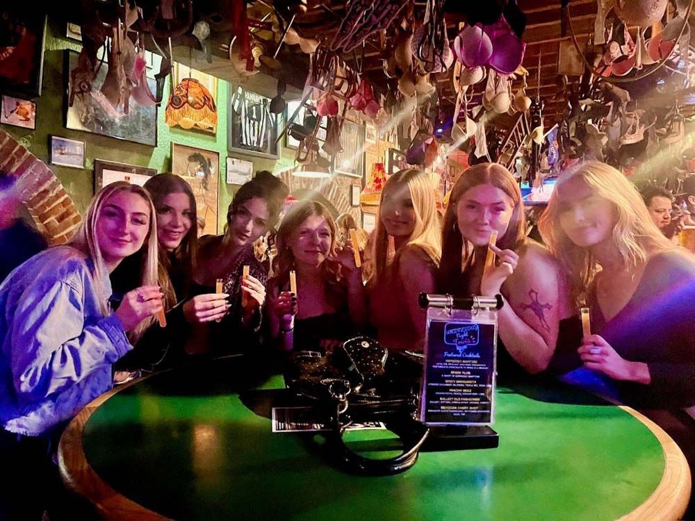 Three women in cowboy hats are sitting at a table in a bar.