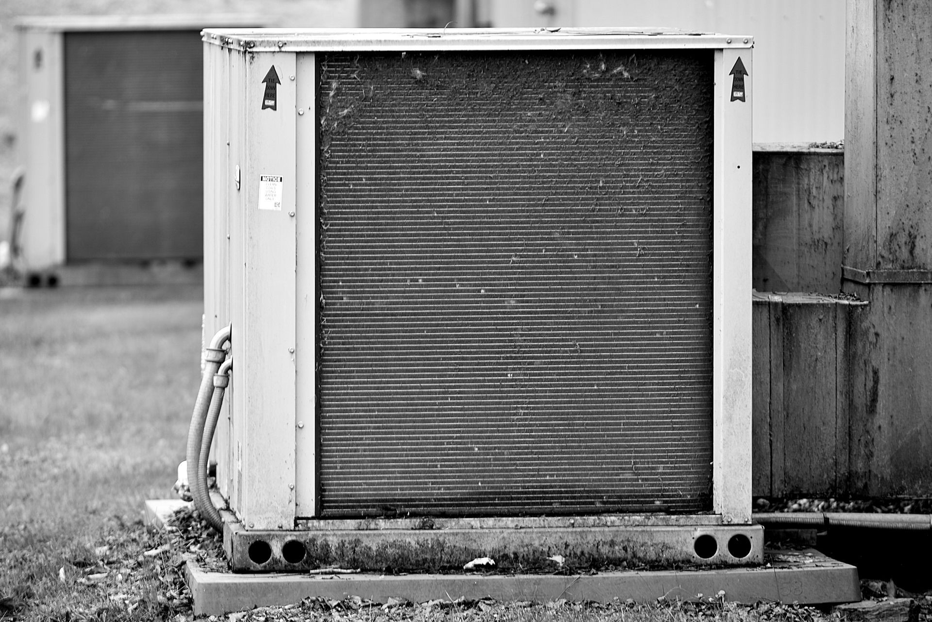 A black and white photo of a rectangular outdoor air conditioning unit sitting on a concrete pad with grass in the background.