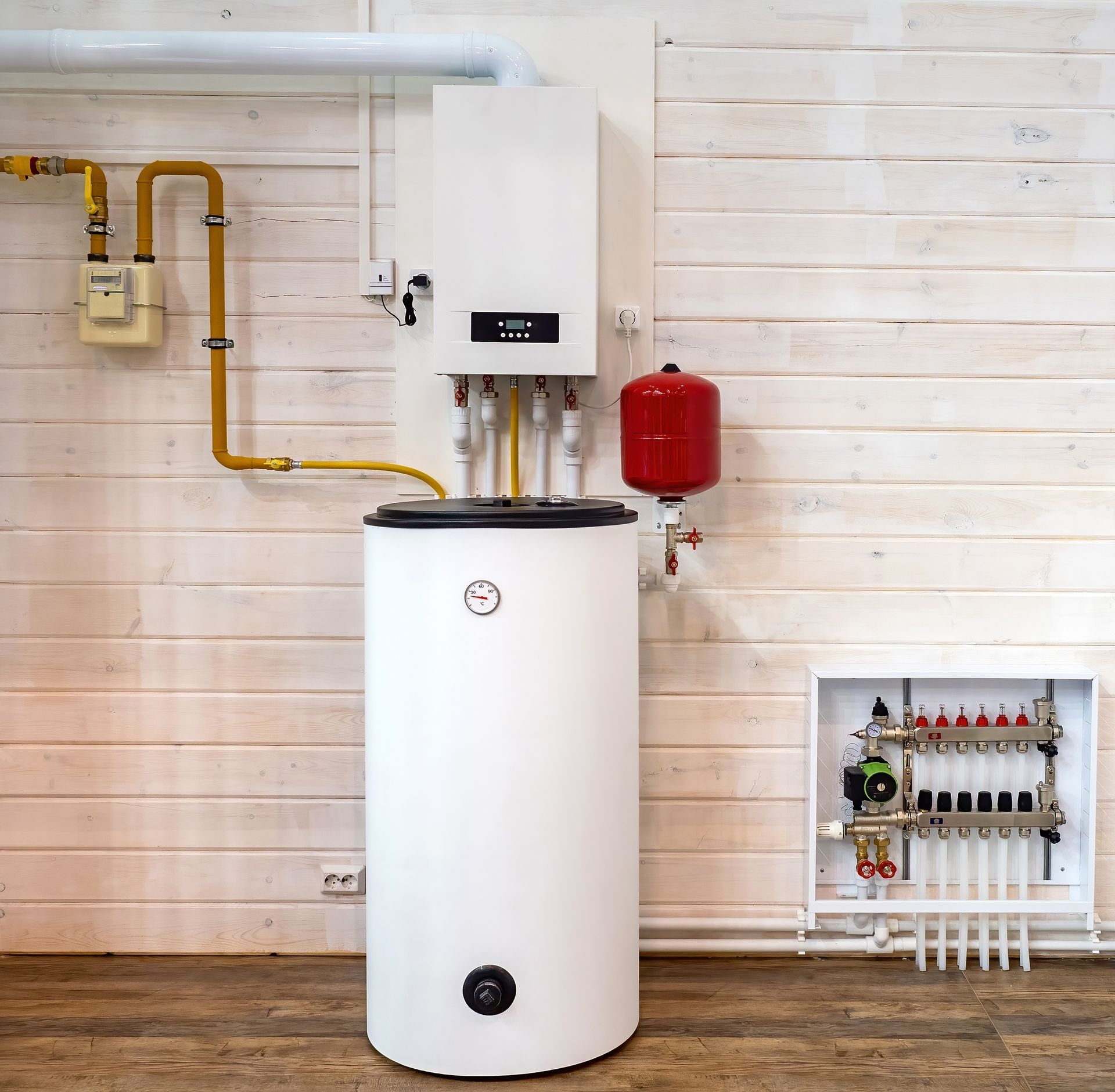 A wall-mounted gas boiler, a vertical hot water tank, an expansion vessel, and a floor heating manifold in a room.