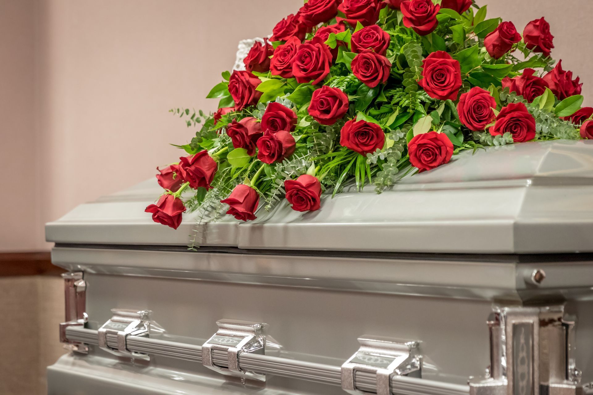 Silver casket topped with red roses in a funeral setting