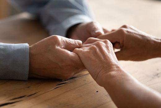 Hands clasped together on a wooden table in a close-up, supportive scene