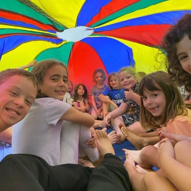 Children gathered under a colorful parachute