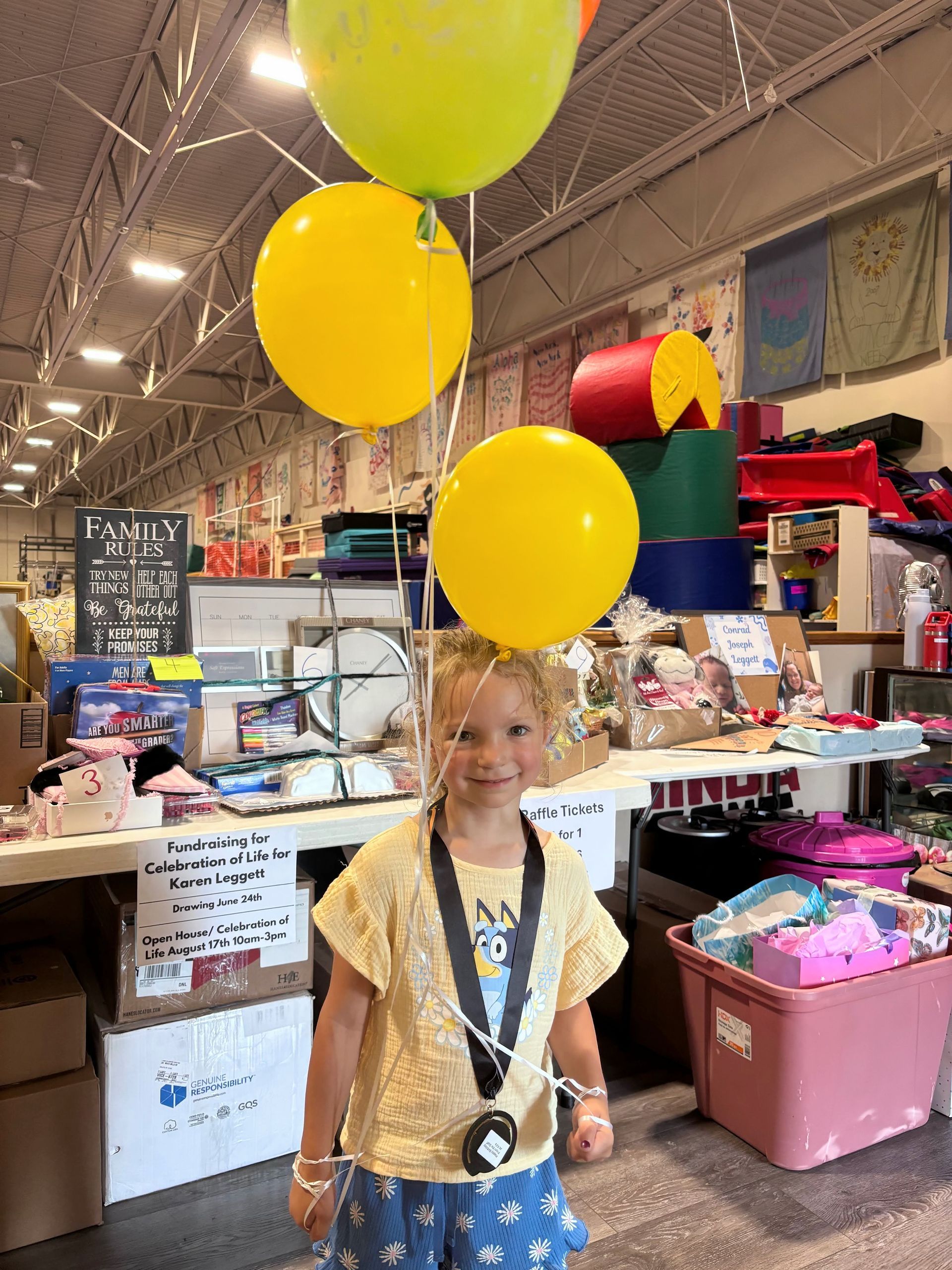 Young girl smiles, holding yellow and green balloons in a store.