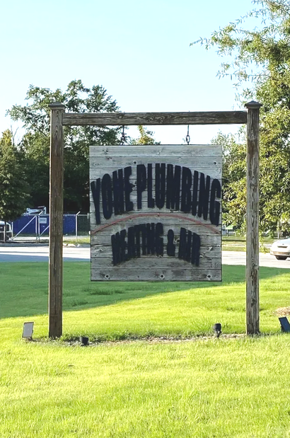 Weathered wooden sign in a grassy roadside area, partially reading “... Plumbing” and “... Since 19...”