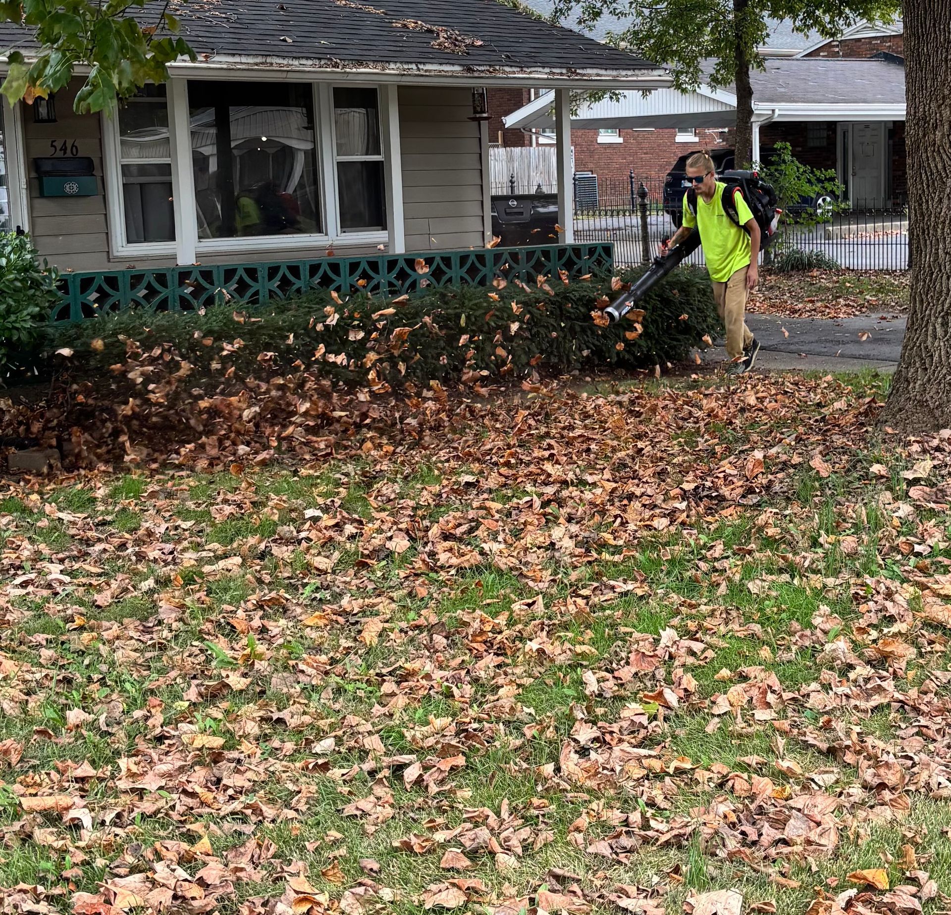 Two men tending a trailer with landscaping equipment in front of a brick apartment building under a blue sky.