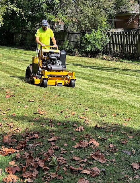 Black truck with lawn care equipment parked on green grass near a tree and houses.
