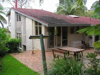 House with red tile roof, white walls, and outdoor patio with table and chairs. Surrounded by greenery.
