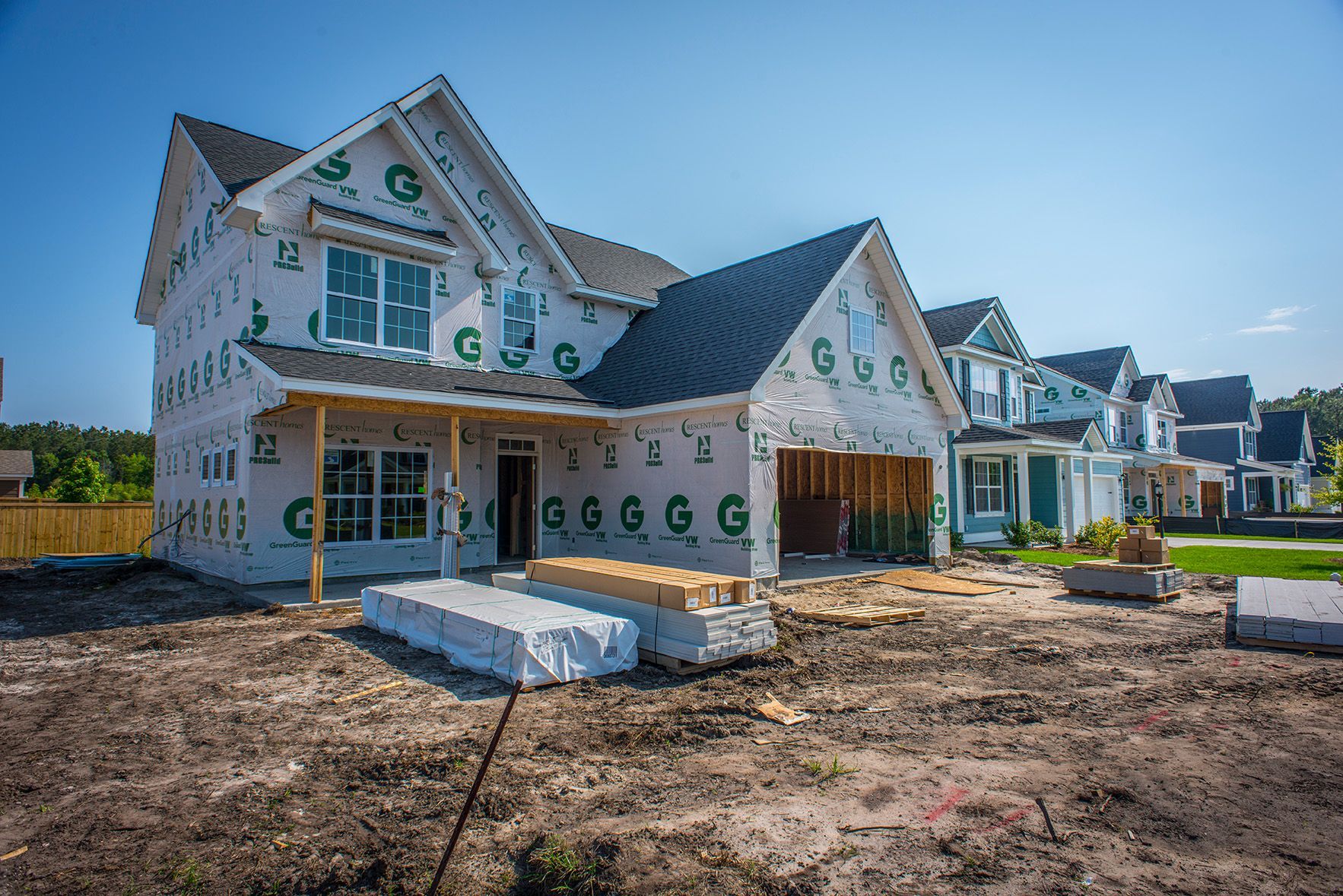 New home construction; house wrapped in green-logoed paper; blue sky; other homes in background.
