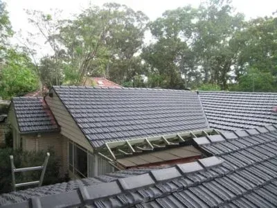 Rooftop with gray tiles being worked on; trees in background.