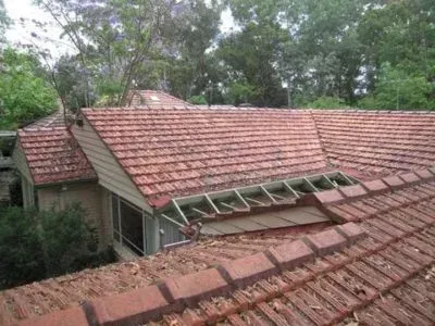 Red tile roof on a house with visible beams, surrounded by trees.