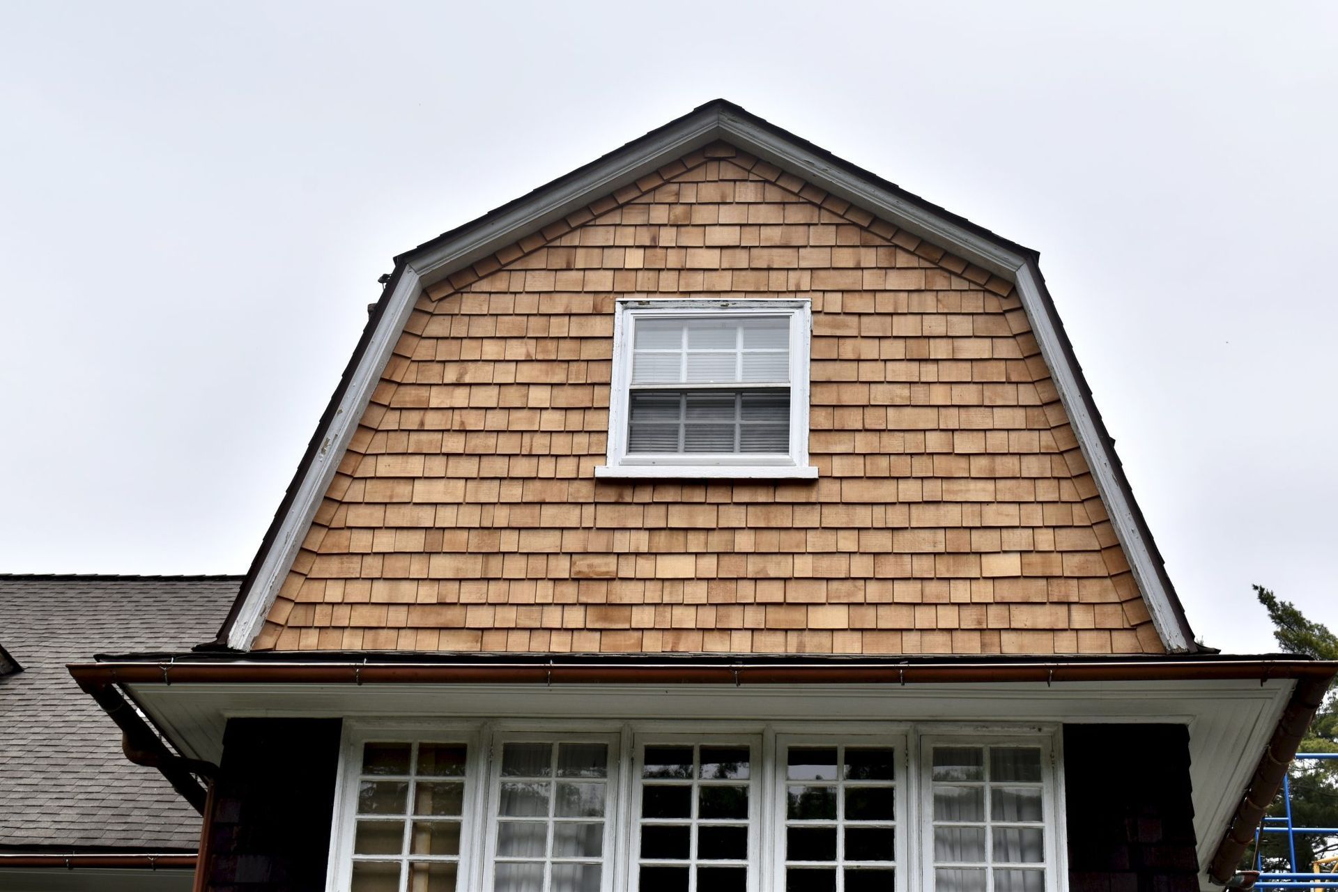 A house gable with cedar shake siding, a window, and brown trim under a cloudy sky.