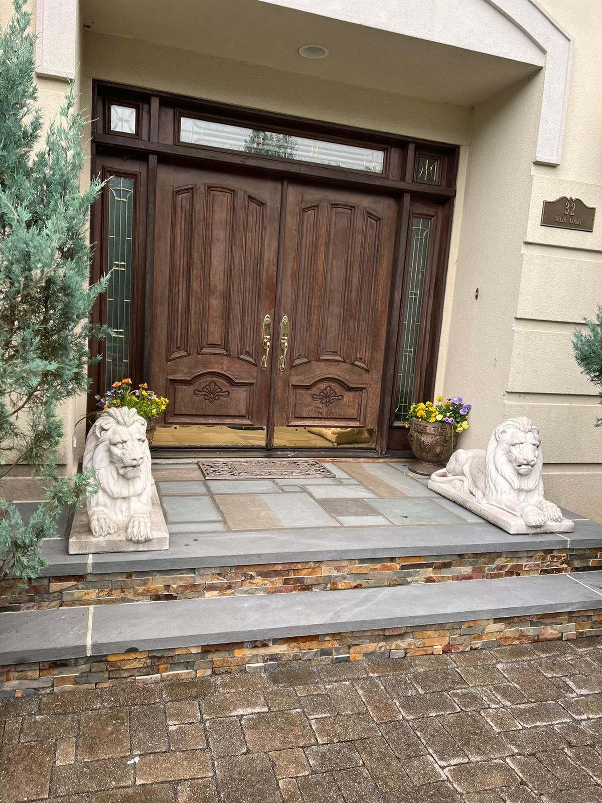 Front entrance with double wooden doors, stone steps, lion statues, and potted plants.