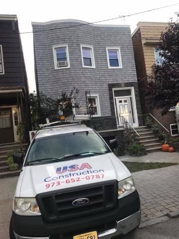 White Ford truck parked in front of a gray house with air conditioning units and a white door.