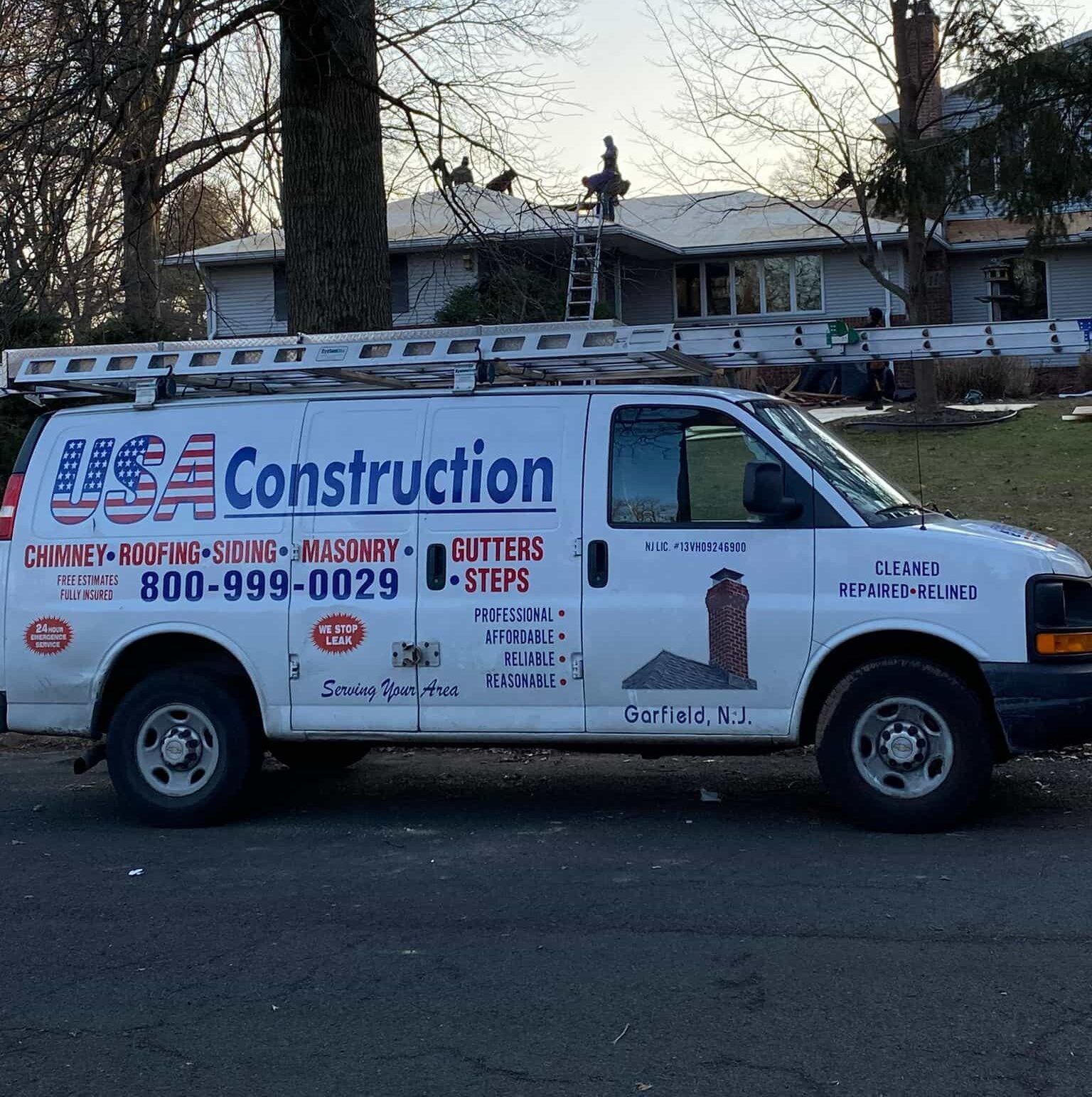 White USA Construction van with ladder parked in front of a house, roofing work in progress.