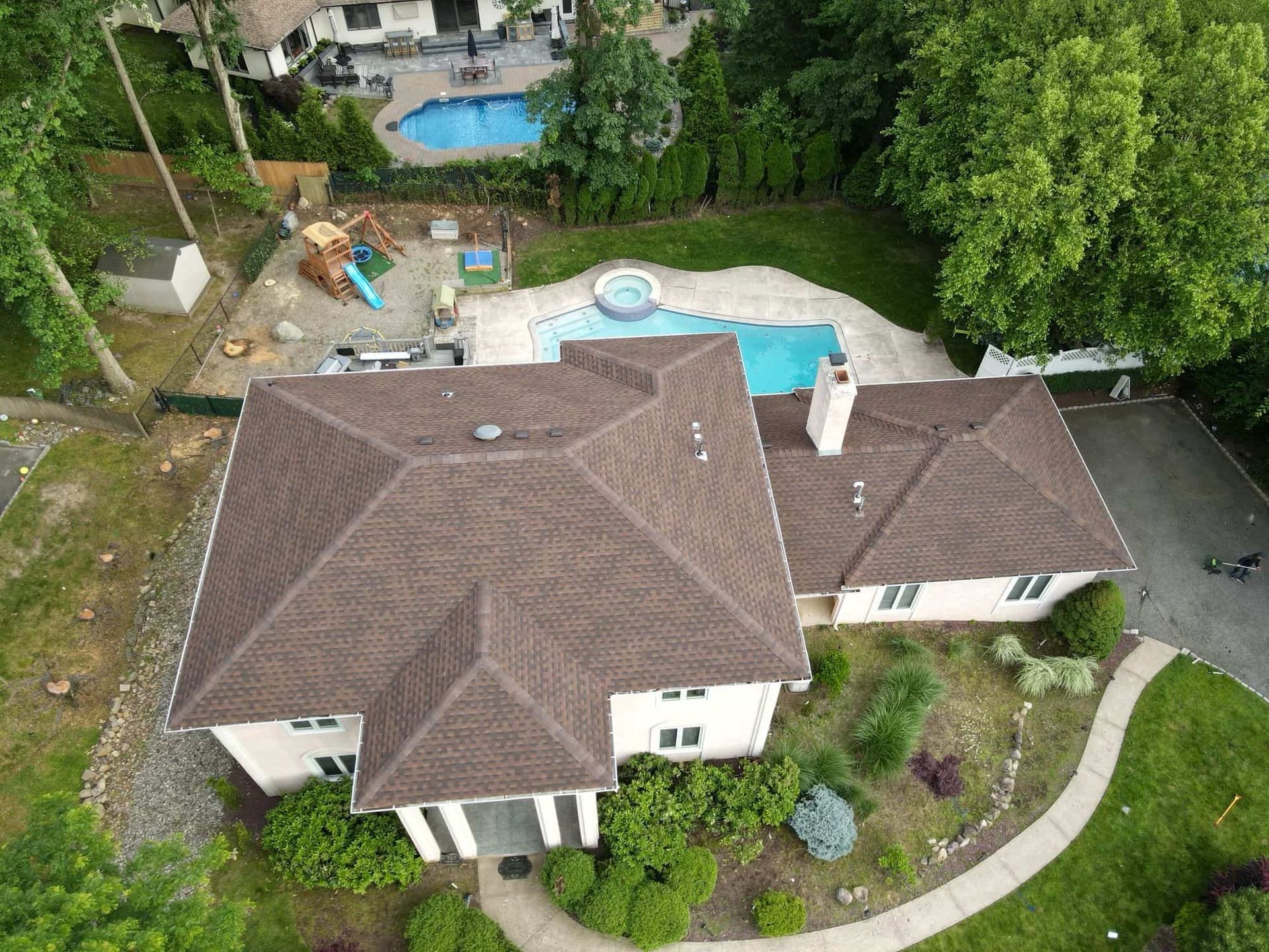 Aerial view of a house with a brown roof and a pool in the backyard surrounded by trees.