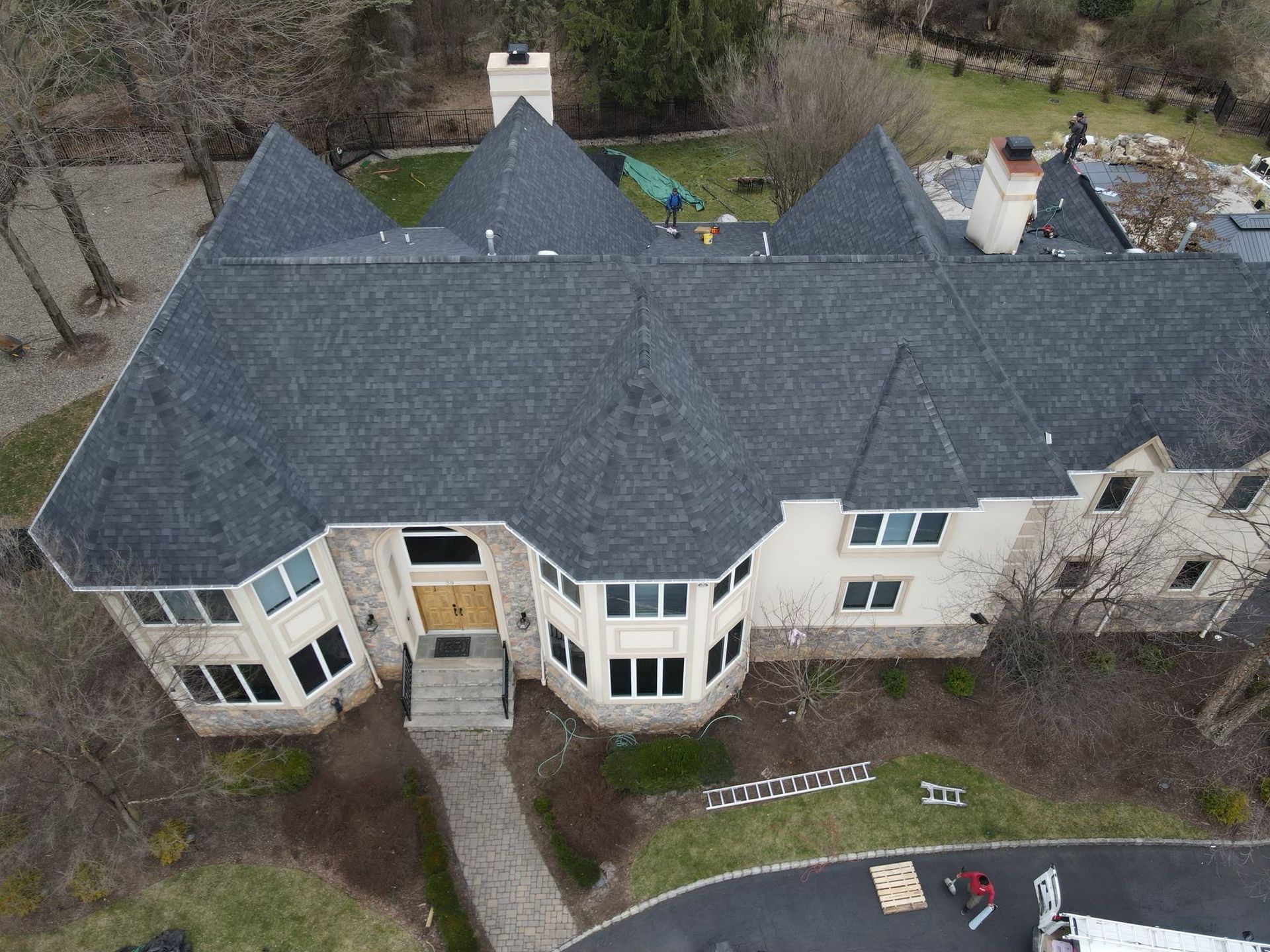 Large house with dark gray shingle roof, multiple gables, and stone facade. Entryway and driveway visible.