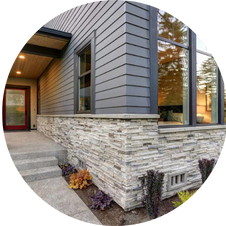 Exterior corner of a modern house, gray siding, stone facade, large windows.