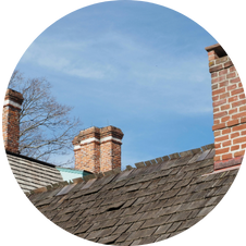 Brick chimneys on a weathered wooden shingle roof against a blue sky.