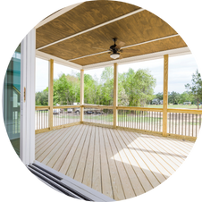 Wooden porch with ceiling fan overlooking a grassy area and trees.