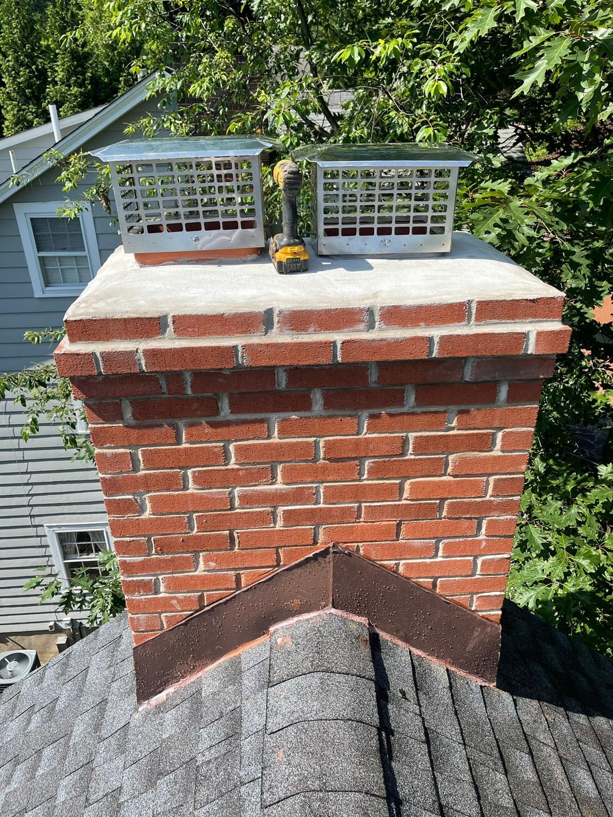 Brick chimney with two metal chimney caps on a roof.