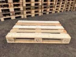 A wooden pallet is sitting on the ground in front of a pile of wooden pallets.