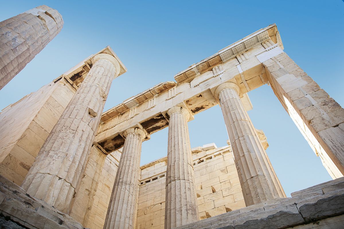 Low-angle view of ancient marble columns from the Parthenon in Athens against a clear blue sky.
