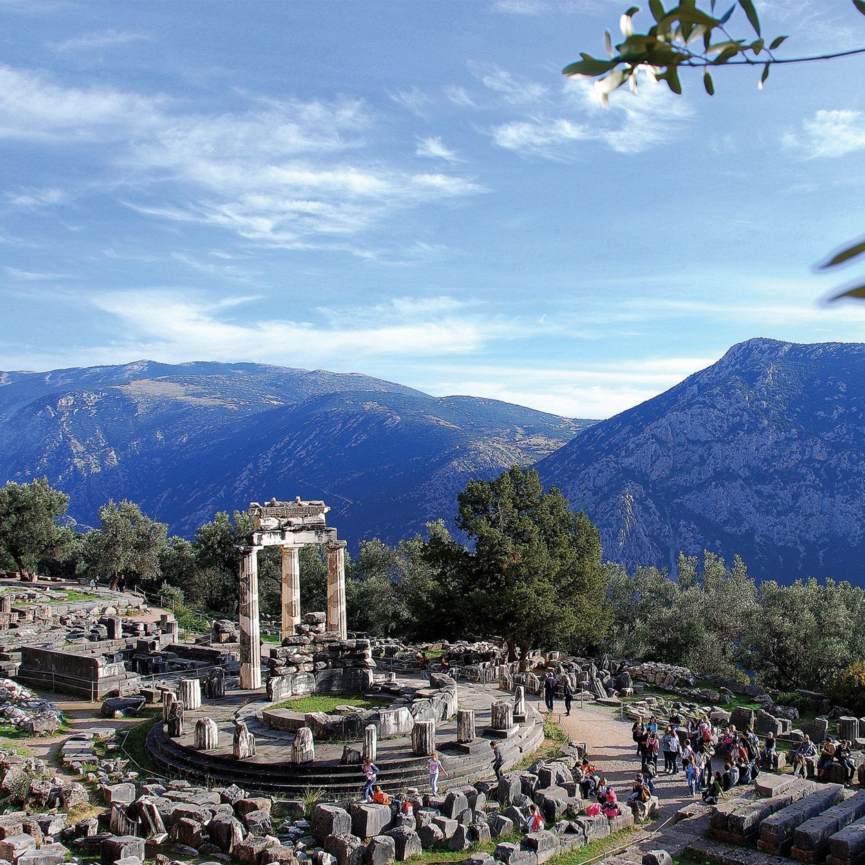 The Tholos of Athena at the ruins of Delphi, Greece, featuring ancient stone columns set against a mountain landscape.