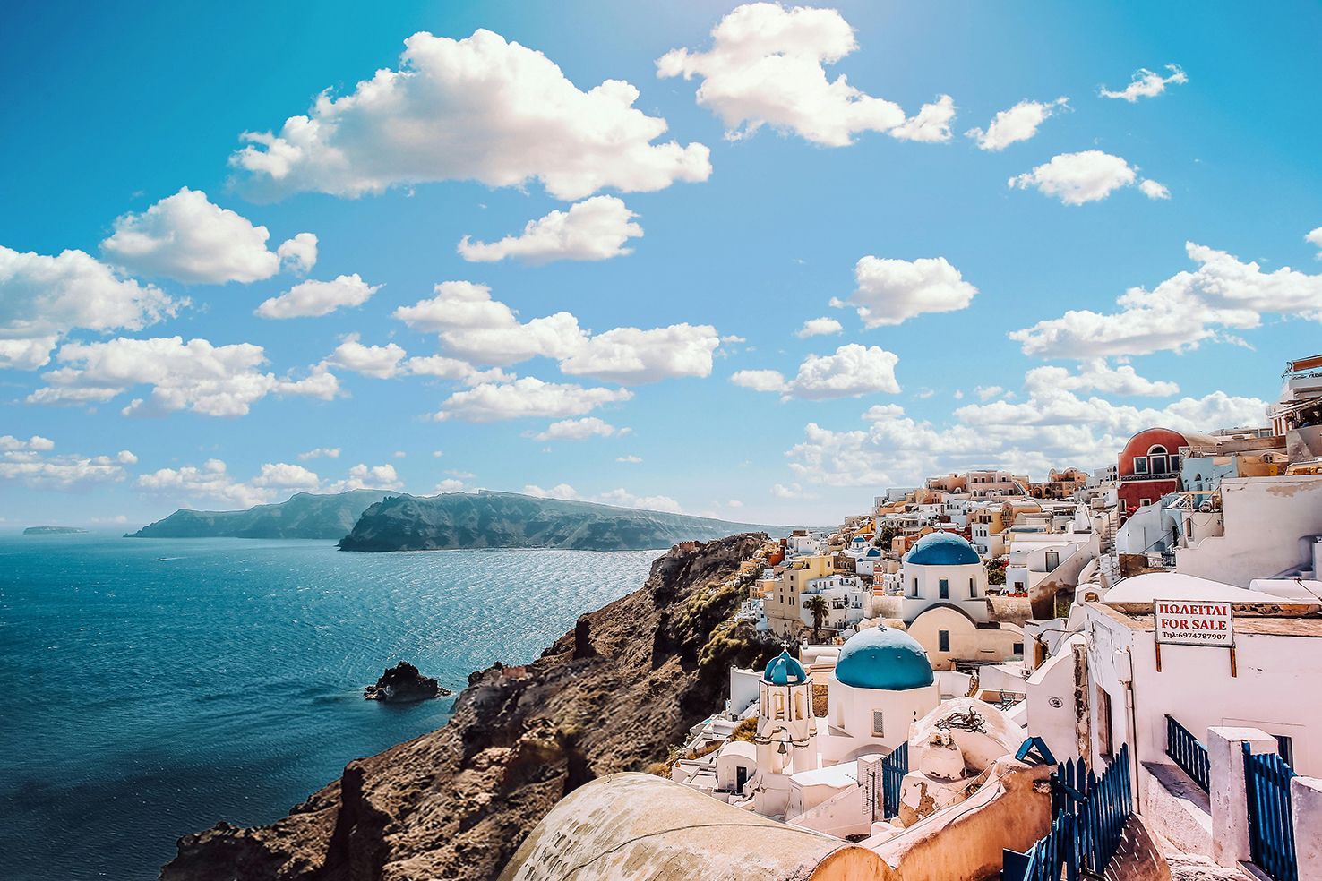 A scenic view of Oia, Santorini, featuring white buildings with blue domes perched on a rocky cliff overlooking the sea.
