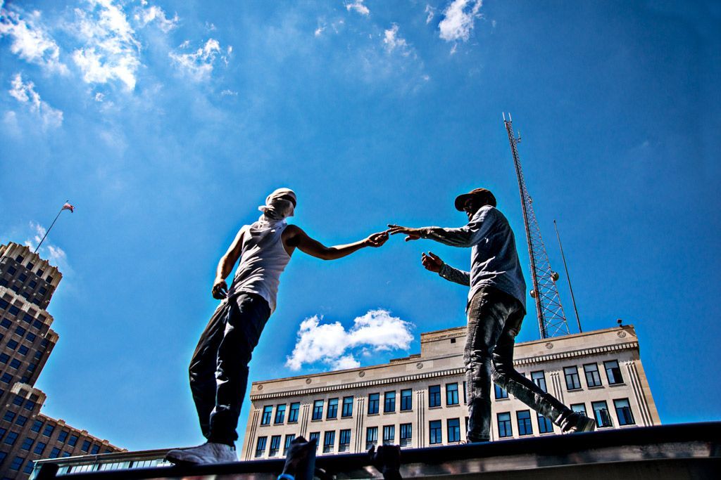 Two protesters touch fingers in a Michelangelo “Sistine Chapel & David” moment as they stand atop a public bus shelter in downtown St. Louis to lead chants during the Stockley protests there. Photographed on September 15, 2017.