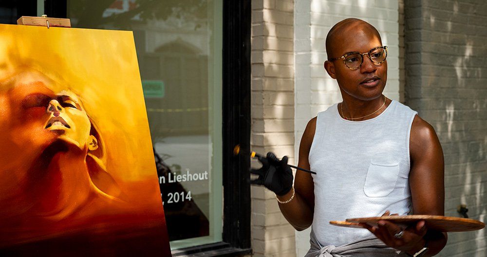 African American  man is holding a palette in front of a painting of a woman in front of the Duane Reed Gallery on McPherson Avenue in St. Louis' Central West End.