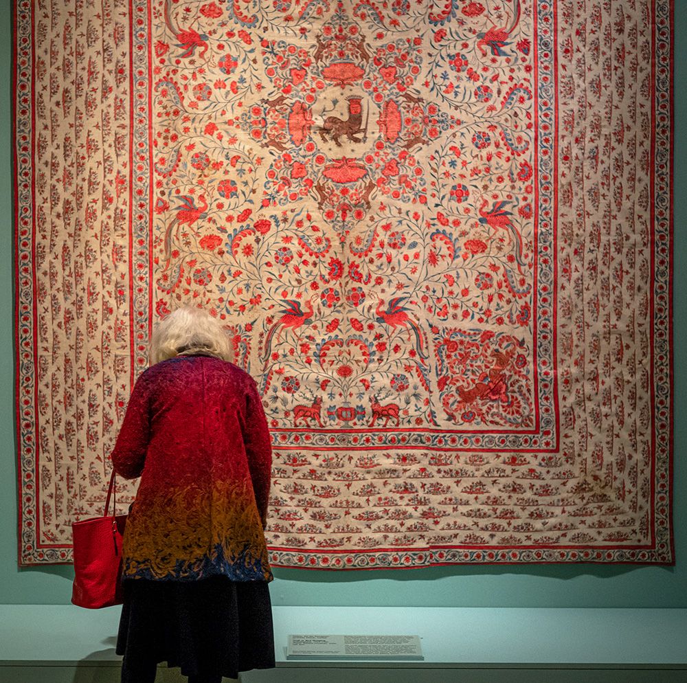 a woman in a red coat is looking at a rug in the 2022 exhibit on tapestries at the St. Louis Art Museum (SLAM) located in Forest Park, St. Louis, Missouri.