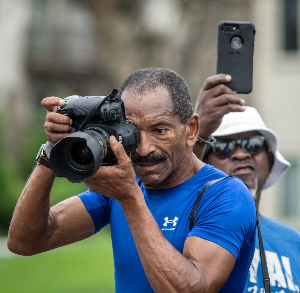 Wiley Price, staff photographer for the St. Louis American newspaper in St. Louis, Missouri, photojournalist,  in a blue shirt is taking a picture with a Nikon D850 DSLR camera at the 9th Anniversary of Michael Brown's murder in Ferguson, Missouri.