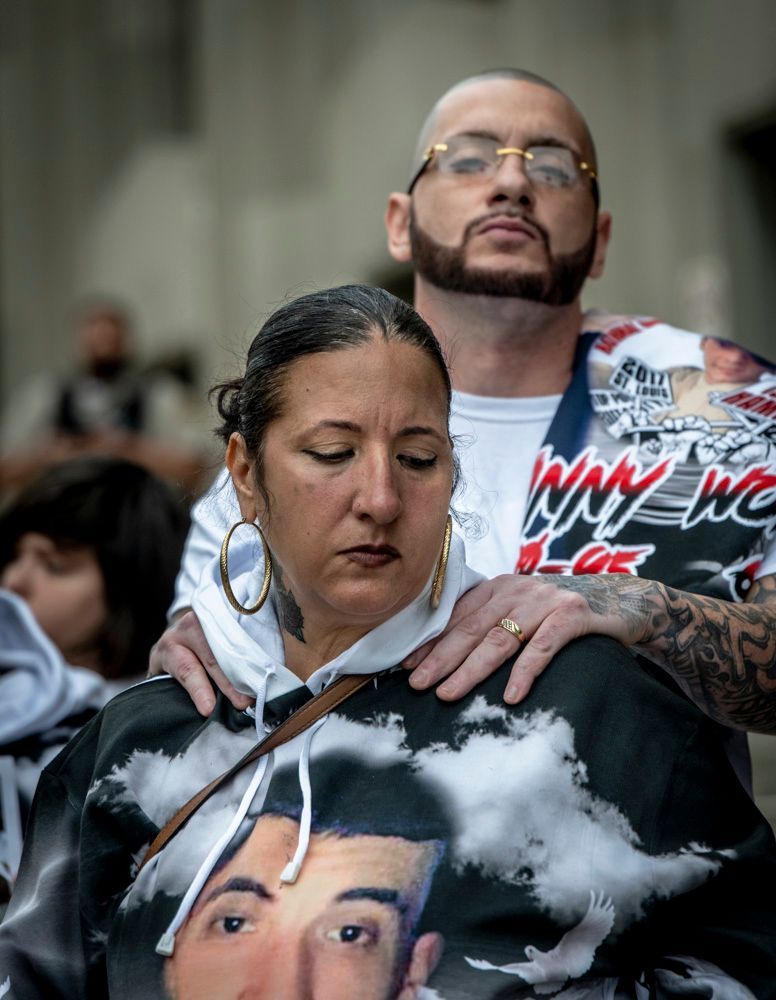 a husband and wife are hugging and the man has his hands on the woman's shoulders to console her as they mourn the shooting of their son by a police swat team who entered her father's home and shot their son who was unarmed.