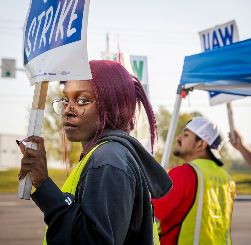 a woman is holding a picket sign that says strike, UAW worker on strike at Wentzville, MO GM assembly plant, October, 2023, dyed red hair, United Auto Workers union