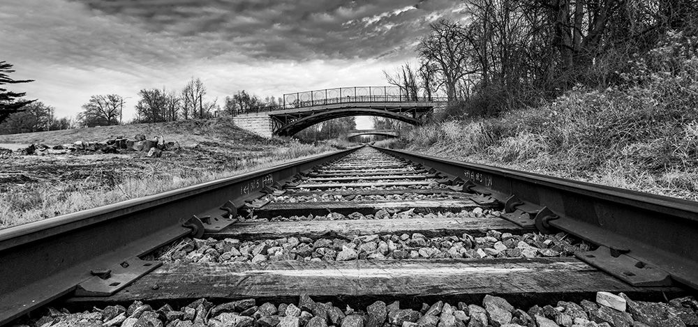 a black and white photo of train tracks with a bridge in the background . In Carondelet Park, St. Louis, Missouri, Nikon D850 with Tokina 16-28mm f2.8 lens. 