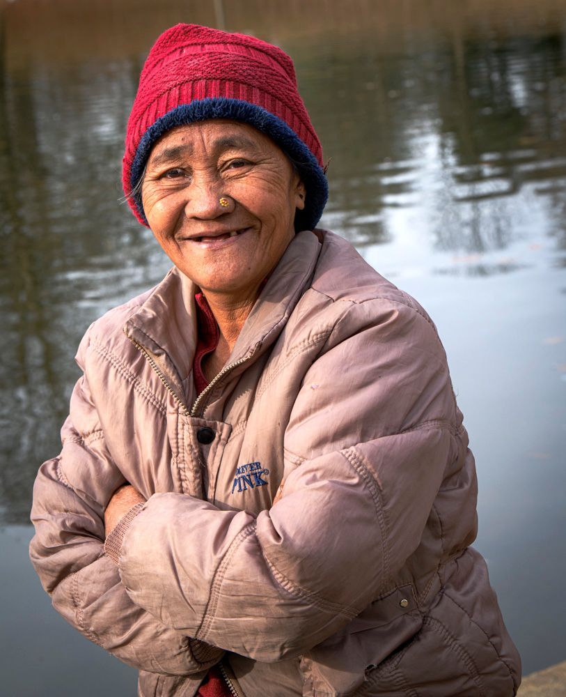 a woman wearing a red hat and a jacket is standing on the bank of the main lake in Carondelet Park, often referred to as the Boathouse Lake. She was with her son fishing for trout, which is stocked in the lake during winter months. She is of Asian descent.