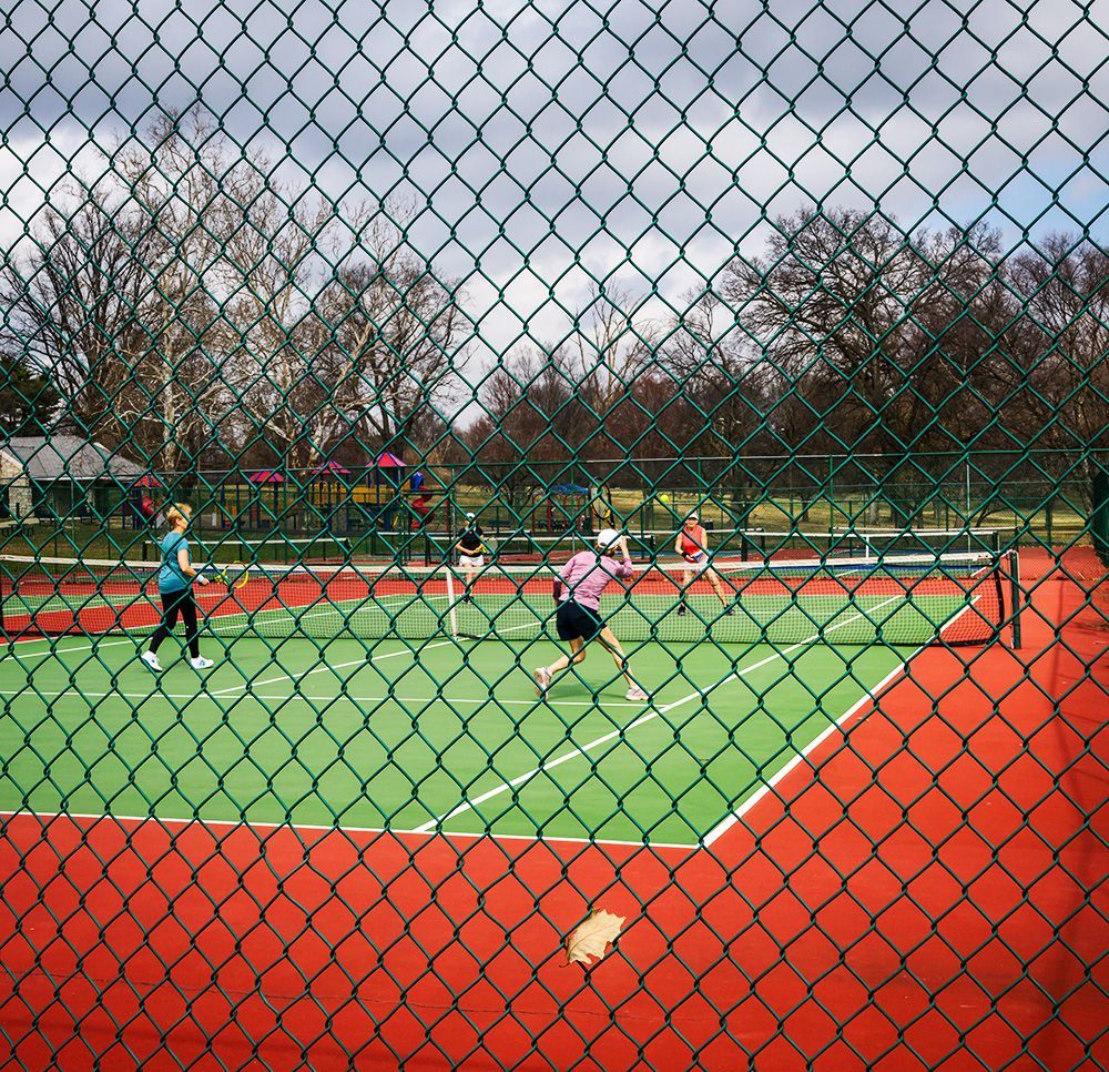 four senior women playing tennis on a tennis court behind a chain link fence in Francis Park, St. Louis, Missouri