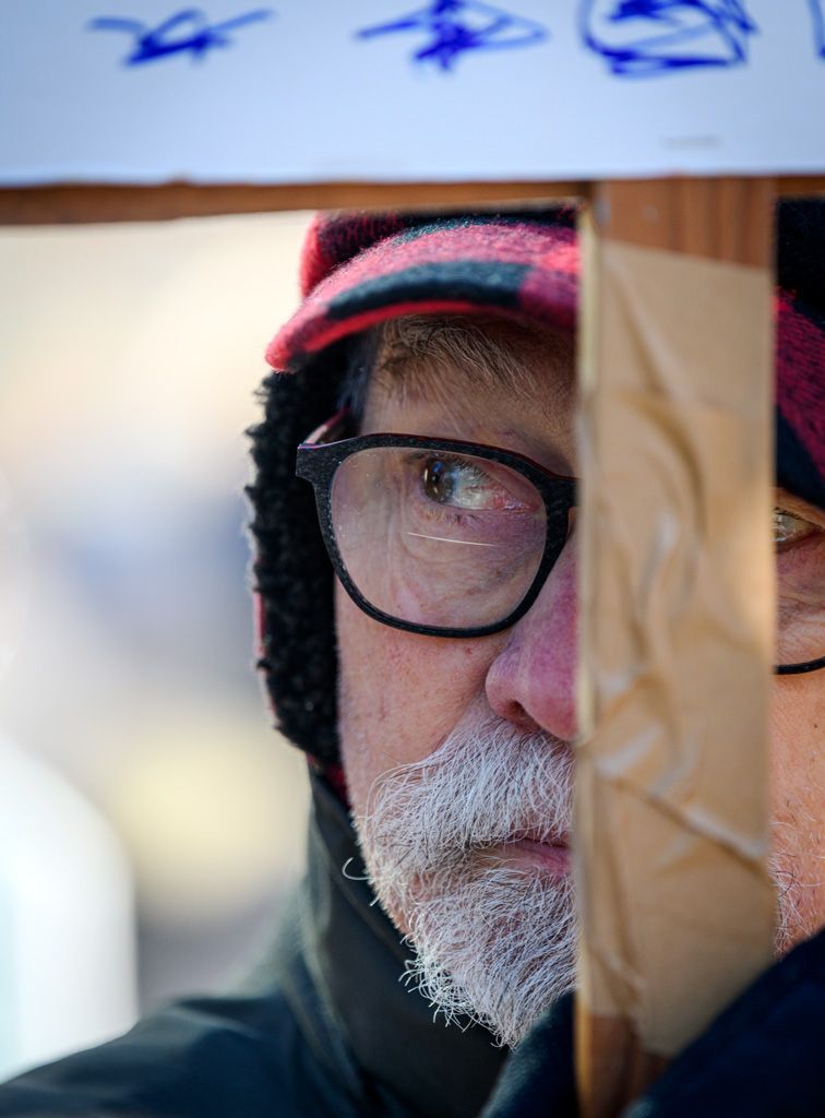 A protester peers from behind his sign, objecting to the murder of Renee Nicole Good in Minneapolis, Minnesota. Demonstrators were not joyous on this day and exhibited both mourning and anger that this is happening in America — so reminiscent of bygone slave patrols and gestapo tactics in Nazi Germany. Photographed on January 11, 2026. 