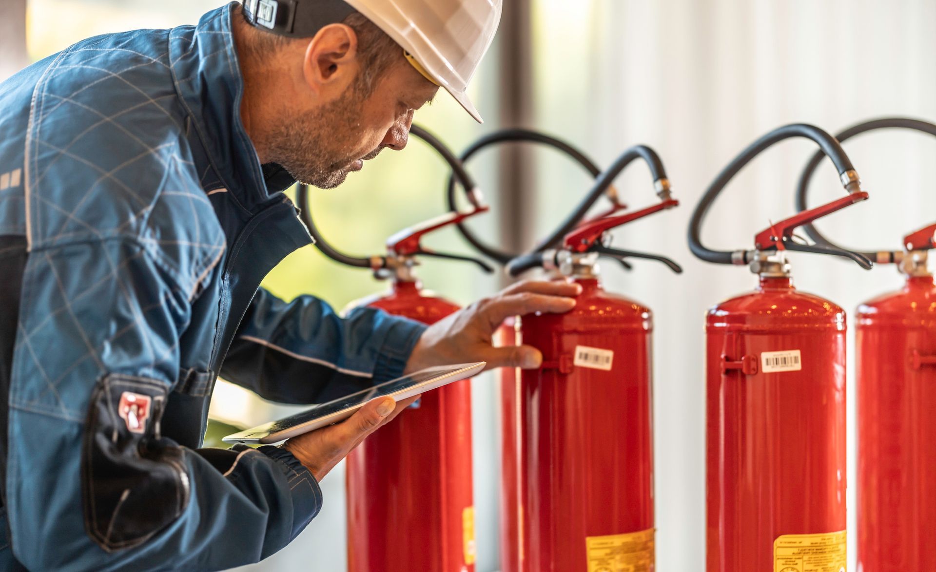 Person inspecting red fire extinguishers while holding a clipboard.