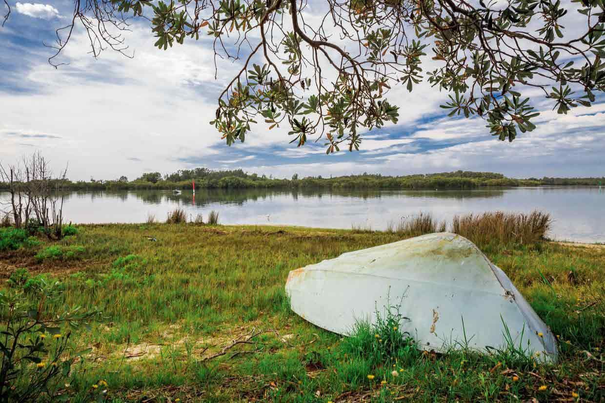 A White Boat Is Sitting On The Shore Of A Lake — Mid Coast Boundary Fencing In Taree, NSW
