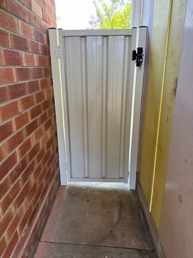 A White Gate Is Sitting Next To A Brick Wall — Mid Coast Boundary Fencing In Old Bar, NSW