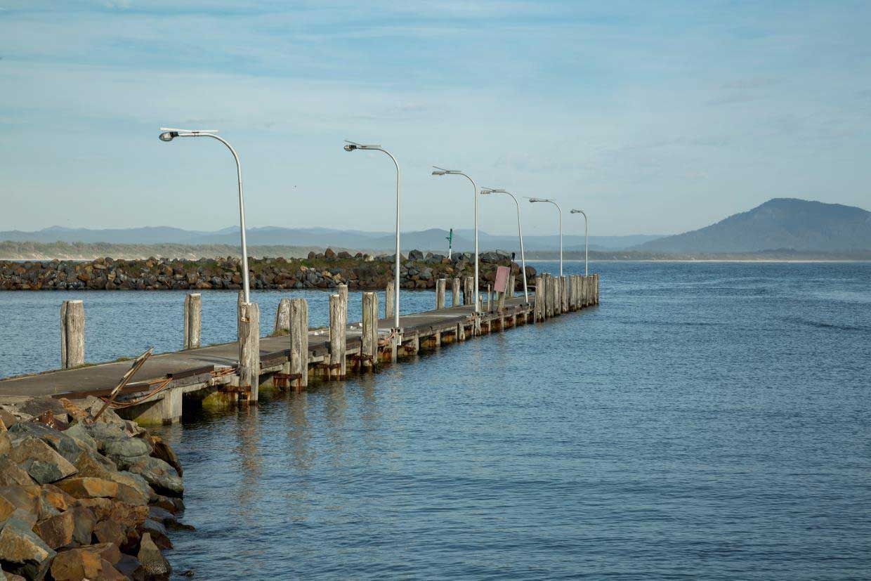 A Dock Leading Into A Body Of Water With Mountains In The Background — Mid Coast Boundary Fencing In Taree, NSW